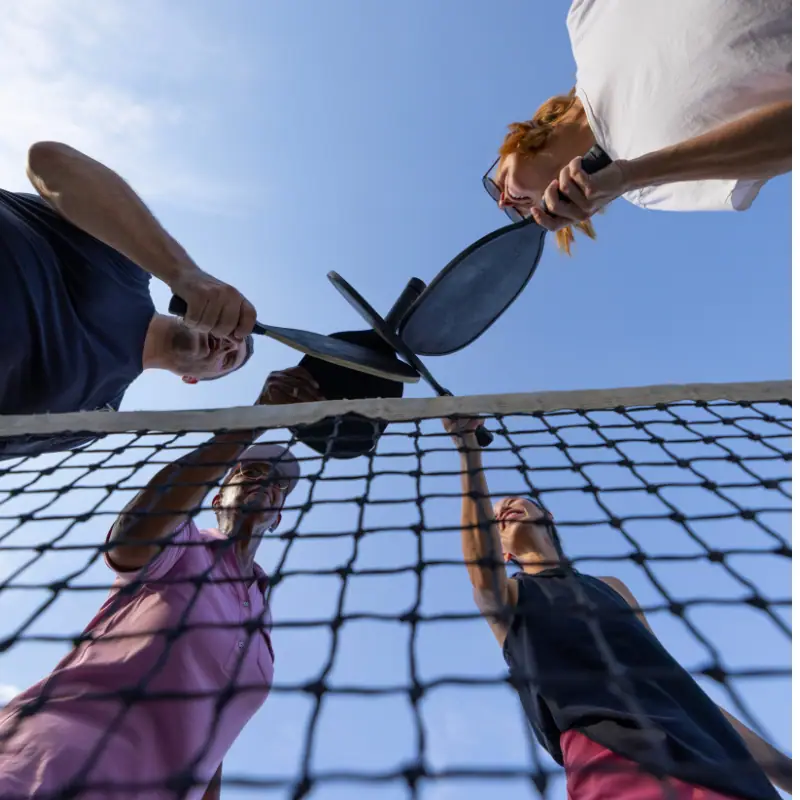 Four neighbors bringing their paddles together over a pickleball net